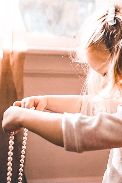Portrait photo of young Anna holding pearl necklace out stretched